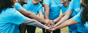 Happy group of volunteer people stacking hands celebrating together outdoor - Teamwork and charity support concept - Focus on back faces